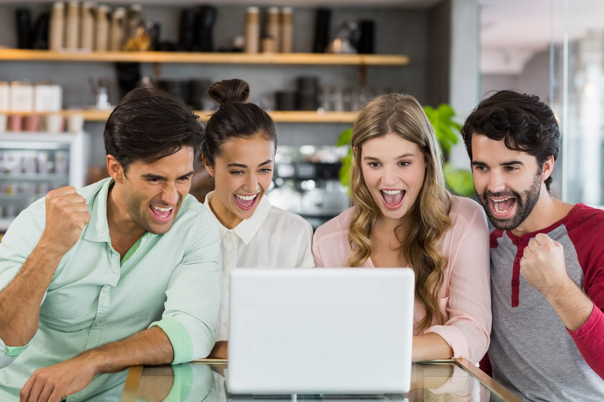 Grupo de amigos sorridentes reunidos em volta de um laptop, demonstrando entusiasmo e colaboração em um ambiente descontraído