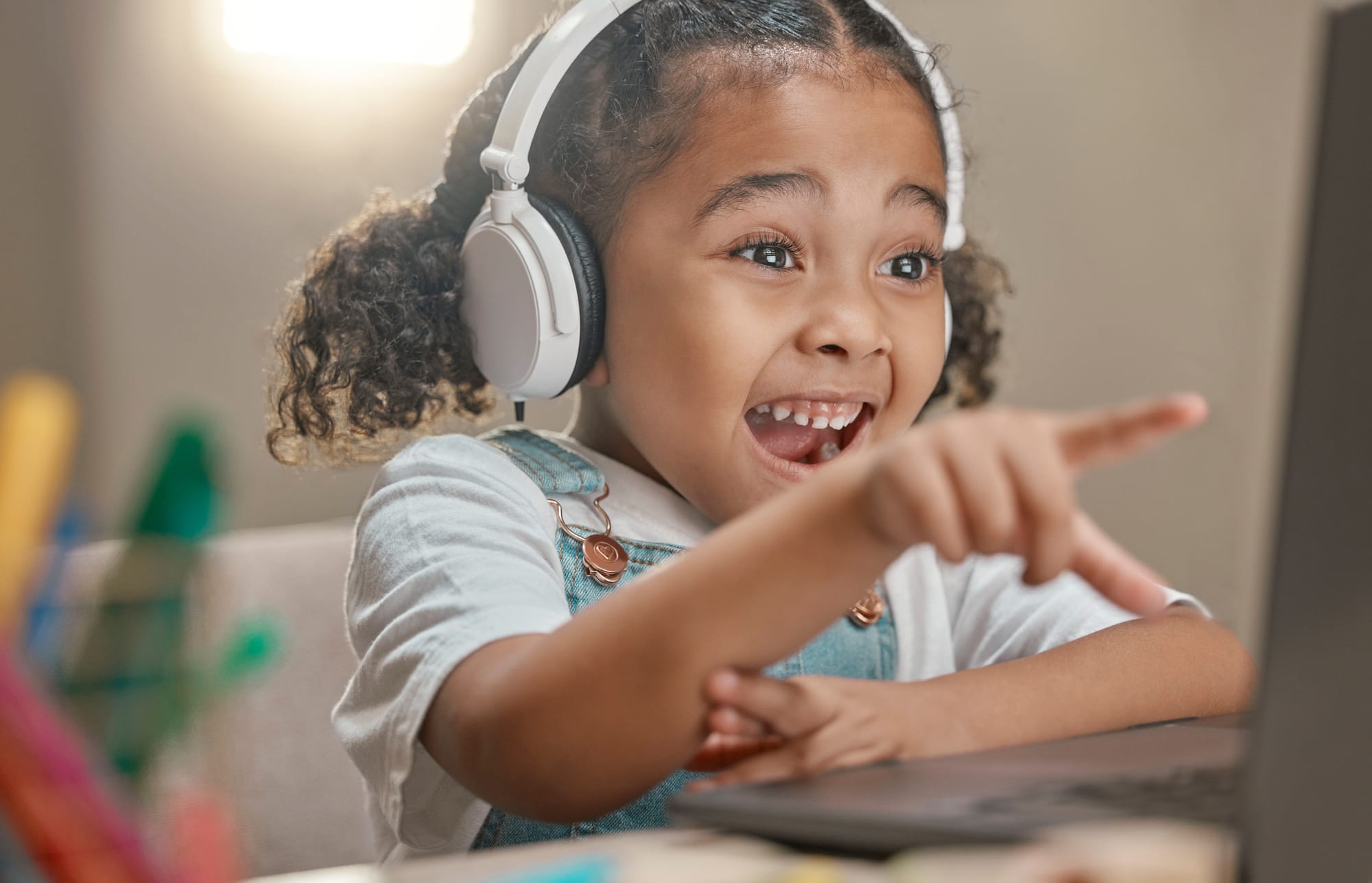 Garota sorridente usando laptop e fones de ouvido em casa, representando o aprendizado remoto e o uso da tecnologia na educação infantil.